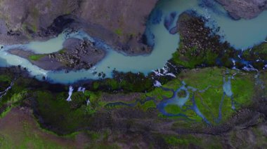 Havadan bakıldığında, karanlık volkanik kayalar ve İzlanda 'daki yeşil yosunlarla örülmüş sütlü turkuaz eritilmiş su, gün ışığında küçük şelaleleri gösteriyor..