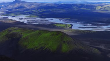 Havadan bakıldığında, volkanik kraterler örülmüş bir buzul nehri ve İzlanda dağlarında yumuşak gün ışığı ve yavaş bir panoramik uçuşla siyah kum düzlükleri görülüyor..