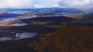 Merkezi İzlanda Highlands üzerinde hareket eden hava manzarası karanlık bir krater, turkuaz bir krater gölü, örülmüş buzul nehirleri ve yumuşak gün ışığı altında paslı yamaçlar gösteriyor..