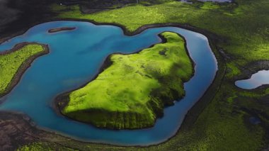 Hava eğimli tavası, İzlanda volkanik ovasında yosun tepesi etrafında kıvrılan bir turkuaz buz kanalı gösteriyor. Sığ havuzlar, lav dokuları ve düşük açılı ışık..