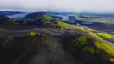 İzlanda volkanik dağlık arazisi üzerindeki hava aracı taraması kül konileri, krater jantları, karanlık lav düzlükleri, örülmüş nehirler, gölcükler, yumuşak bulutlu ışık gösteriyor.