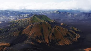 İzlanda 'daki hava araçları çok renkli rhyolit çıkıntıları, kraterli zirveleri, siyah kül ovaları, örülmüş nehirleri ve yumuşak ışık altında koyu lav tarlaları olan Landmannalaugar dağlarını gösteriyor..