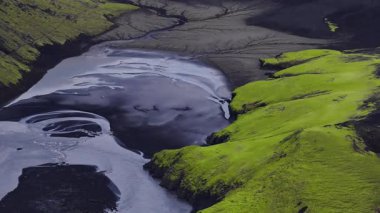 Düşük hava görüntüsü karanlık volkanik kumun üzerinde örülmüş buzullu kanallar dik tepelerde neon yosunları yansıtıcı su girdapları ve İzlanda 'da taze gün ışığı dokuları gösteriyor..