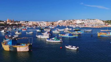 Kubbeli bir kiliseyle Malta 'daki Marsaxlokk limanının havadan görünüşü, birçok luzzu ve küçük tekne derin mavi sularda sallanıyor, parlak gün ışığı parlak renkler ve berraklık gösteriyor..