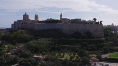 Malta 'daki Mdina üzerinde hava manzarası perde duvarlarını, St. Paul Katedrali' ni, terasları, surlardaki ziyaretçileri, palmiye ağaçlarını ve kırsal bölgeyi yumuşak öğleden sonra ışığında gösteriyor..