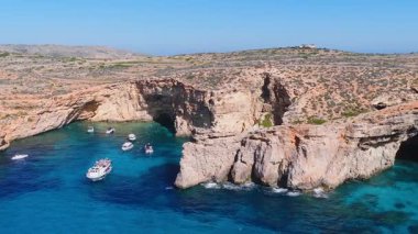Kireçtaşı kayalıkları, kemerleri, deniz mağaraları, canlı mavi sular, yatlar ve tur botları, yüzücüler ve güneş banyosu sunan Comino Blue Lagoon, Malta 'nın öğlen hava manzarası..