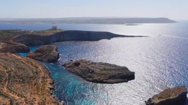 Comino, Malta havadan bakıldığında Saint Mary Kulesi, kireçtaşı uçurumları, adacıklar, turkuaz körfez, yatlar ve yüzücüler korunaklı sularda gün ışığının keyfini çıkarırken tekneler görülüyor..