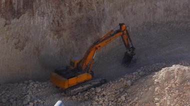 Hava görüntüsü, Malta 'nın Mellieha kentindeki kireçtaşı ocağında Hyundai kazıcısının kayayı hareket ettirdiğini gösteriyor. Sıcak gün ışığı, soluk taş, temiz izler, boru ve yuvarlak taş yığınları..