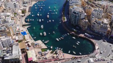 Sliema 'nın parlak hava manzarası, Malta kavisli bir iskele, soluk kireçtaşı daireler, balıkçı tekneleri ve eğlence gemileri, otobüsler ve yaya geçitleri gösteriyor..
