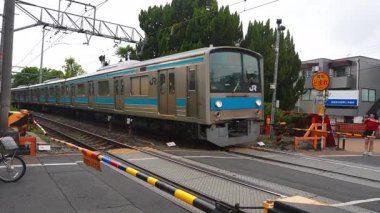 JR treni Kyoto, Japonya 'daki bir geçitten geçerken katenareri kablolarının altında trafiği tıkayan Kyoto' yu işaretledi. Yayalar bulutlu ışıkta turuncu dur işaretinin yanında beklerler..