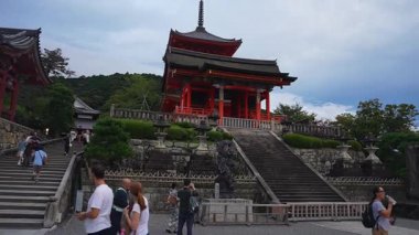 Japonya 'nın Kyoto kentindeki Kiyomizu derasının gün ışığında ziyaretçiler yürürken, fotoğraf çekerken ve tırmanırken kırmızı pagoda, taş teras, fener ve dik merdivenlerle gündüz görüşü..