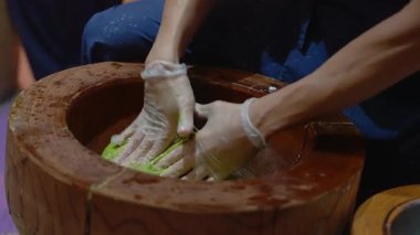 Eldivenli eldiven ile yoğurulan parlak yeşil mochi Kyoto 'da oyulmuş ahşap bir usu, bastırma, katlama ve durulama hareketleri, sığ alan derinliği, sıcak ışık.