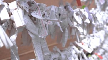 Kapalı tavada Tokyo 'daki bir Shinto türbesindeki askıya bağlanmış beyaz omikuji sıraları görülüyor. Kırmızı kenarlı kaymalar, kanji, yumuşak bokeh, sıcak duvar, sığ alan derinliği.