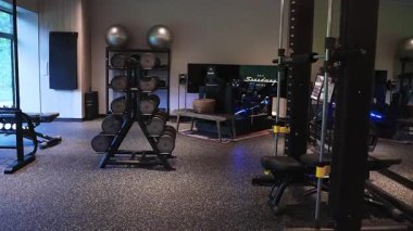 Fuji Speedway Oteli 'nin ışıklandırılmış spor salonunda halterler, kettlebells, bank, güç rafı, egzersiz topları ve Recaro koltuğunda çoklu ekran yarış simülatörü görülüyor.