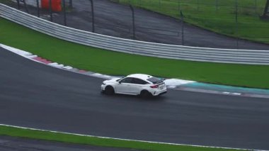 Arka kanadı olan beyaz bir Honda Civic R tipi Bridgestone ve Potenza reklamları olan bir Japon yarış pistinde ıslak bir köşeyi alıyor..