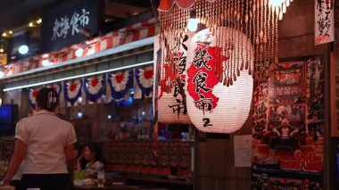 Meşgul bir Tokyo izakaya 'nın dışında yanan fenerleri ve boncuklu perdeleri kapatın. Lokantalar sohbet eder, sunucu geçer, boncuklar sallanır. Sıcak tonlar ve yumuşak bokeh.