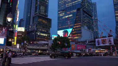 Tokyo 'daki Shibuya Geçidi' nin mavi saati JR girişi, Scramble Meydanı ekranı kalabalıklar otobüs, taksi ve bisiklet geçişi, neon ışıklı kuleler..