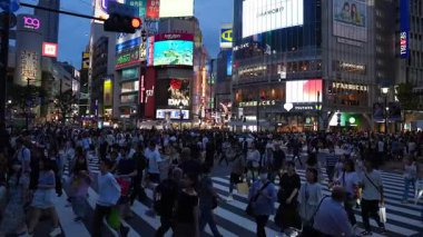 Shibuya 109, Tsutaya Starbucks, H ve M, Rakuten tabelaları, taksiler, arabalar, scooter ve serin neon ışıklarıyla, gün batımında Tokyo 'da Shibuya Geçidi' nden kalabalık akıyor..