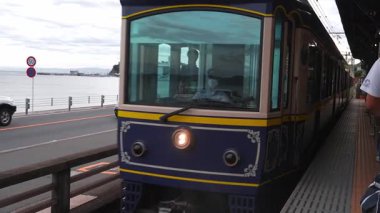 Kamakura işaretli Retro Enoden treni kıyı yolu, arabalar ve bisikletçi geçidi, Enoshima Adası ve Deniz Mumu 'na görünür, bulutlu, kalabalık bir taşıma aracının yanına varır.