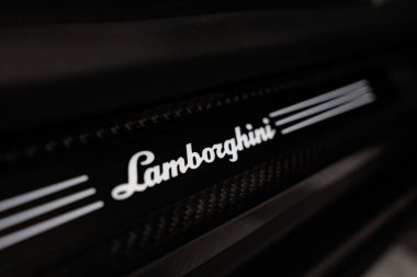 Aydınlatılmış Lamborghini metninin her iki tarafında üç şerit, parlak siyah ve karbon fiber doku, profesyonel bir oto atölyesinde kapalı, yumuşak yönlü ışık