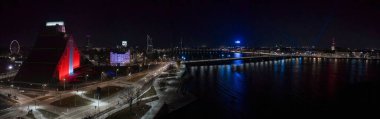 Riga, Letonya geceleri Daugava Nehri, Stone Köprüsü ve Riga Ulusal Kütüphanesi 'ni gösteriyor. Televizyon kulesi uzak, sessiz sokaklar ve havai fişekler 2025' te parlıyor..
