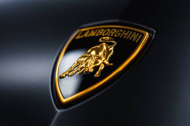 Düşük açılı bir makro, Lamborghini logosunu parlak, karanlık bir panele yerleştirir. Cilalı kenarlar, sığ alan derinliği ve dramatik yansımalarla yumuşak stüdyo ışıklarını yakalıyor..