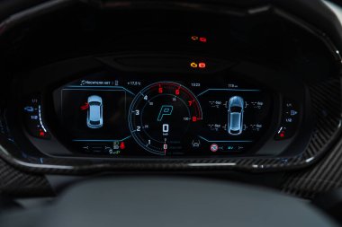 Dijital küme merkezi takometreyi ve Park 'ı gösteriyor, 3 boyutlu araba diyagramları, sıcaklıklar ve uyarılar, karbon fiber süsleme, lüks Lamborghini Urus SE iç mimarisi bir atölye ortamında.