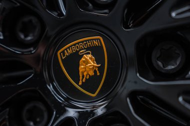 Yakından bakınca, tekerlek merkezindeki siyah bir kalkanda altın bir boğa rozeti, sığ bir alan derinliği, karamsar yansıtıcı aydınlatma, lüks atölye çalışması, hassasiyet odaklı.