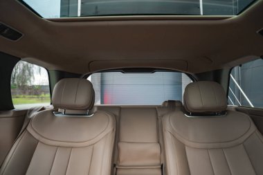 Bronzlaşmış deri koltuklar, heykeltraş başlıkları, arka pencere ve açılır tavan. Yumuşak ışıklandırma dikişleri, krom detaylarını ve dışarıda modern bir tesisi ortaya çıkarır..