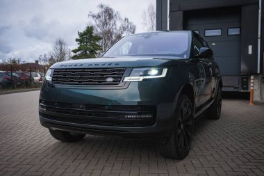 Koyu yeşil Range Rover otobiyografisi bir atölyenin önüne park edilmiş, LED matris farları parlıyor, Land Rover rozeti ortalanmış, alçak açılı görüş bulutlu ışık altında..