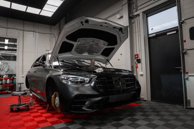 Bir mat siyah Mercedes Mercedes Benz S sınıfı kaputu açık ve kapalı bir servis bölmesi kapağı kapalı oturur panel ışıkları, alet arabası, ve gri duvarlar.