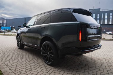 Koyu yeşil Range Rover otobiyografisi modern endüstriyel bir binanın dışındaki tuğla alana park edilmiş. Uzun camları, parlak boyası, siyah tekerlekleri ve gizlilik camları var..