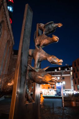 Bremen 'in tuhaf bronz kasaba müzisyenleri Riga Eski Kasabası' ndaki St. Peter Kilisesi 'nin yakınındaki metal bir levhadan alacakaranlık, sıcak ışıklar ve sığ alan derinliği boyunca uzanır..