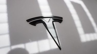 Beyaz boya üzerine siyah Tesla T amblemini kapalı bir sergi salonunda, ince eğim ve tavalarla sığ alan derinliği, görülebilir yansımalar.