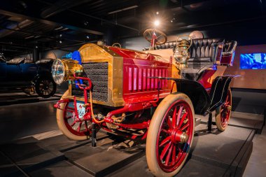 1900 'lerin başında restore edilmiş pirinç bir araba bir otomobil müzesinde, kırmızı gövde ve altın kaplama, bozuk tekerlekler, asetilen farlar, yumuşak koltuklar, dümen dümeni, süslü radyatör..