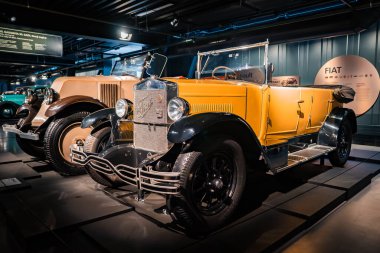 Üzerinde krom detaylar bulunan üstü açık hardal sarısı bir vintage savaş öncesi müze ışıklandırması altında sergilenen bir FIAT sergisinde sergileniyor..