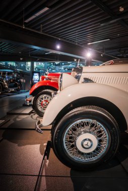 Krem rengi ve kırmızı klasik Mercedes Benz ön çamurluklar ve kasvetli müze ışıklandırması, sergilenen krom ve erken dönem araba çalışmalarının altında açılı platformlar üzerinde tel tekerlekler..