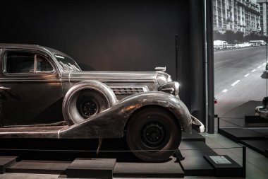 1930 'ların lüks arabasının yan görüntüsü bir otomobil müzesindeki stanchions arkasında. Yedek tekerlek, kapüşonlu kaput ve gözyaşı damlası hafif ışıklandırma ve şehir manzarası altında göze çarpar..