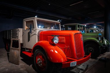 1937 'de yenilenmiş krem taksisi ve kırmızı çamurlukları olan bir kamyon, düşük müze aydınlatması altında yeşil bir dönemin kamyonunun yanında duruyor..