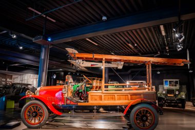 20. yüzyılın başlarında restore edilmiş ahşap panelleri ve çatı merdiveni olan itfaiye aracı bir otomobil müzesinde, pirinç montajı ve kırmızı kaput parıltısında, antika arabaların ötesinde yer alır..
