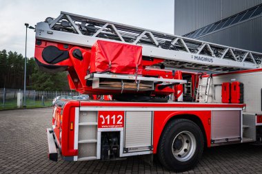 Yakından bakıldığında, Letonya 'daki Magirus itfaiye aracı 32 metre merdiven, 112 numara ve yanında vugd.gov.lv var. Gündüz vakti modern bir sanayi binasının yanına park edilmiş..