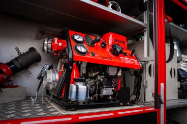 Müzedeki itfaiye istasyonundaki kırmızı taşınabilir itfaiye pompasını kapatın. Göstergeler ve vanalar görünür. Elmas kaplama zemininde hortumlar ve hortumlar.