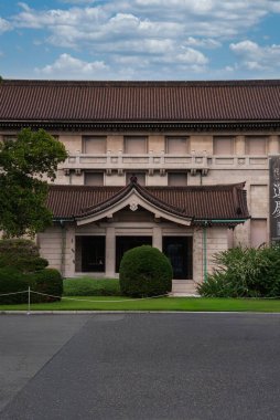 Tokyo Ulusal Müzesi Honkan Ueno Parkı 'nda seramikli çatısı ve çalılar ve çimlerle çevrili simetrik girişi, sakin bir gündüz vakti görüntülenmiştir..