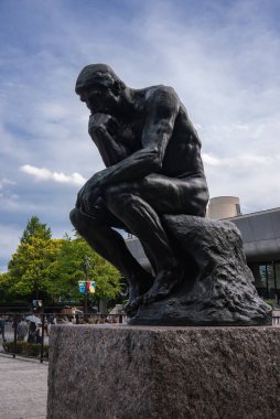Ueno Park, Tokyo 'daki Ulusal Batı Sanatları Müzesi' nin önündeki granit bir kaide üzerinde bronz bir Düşünen. Ziyaretçiler ve ağaçlar plazayı gün ışığında çevreledi.