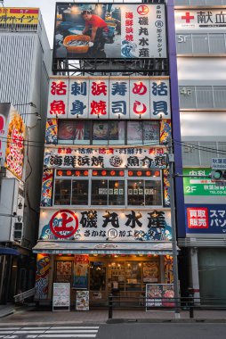 Tokyo 'dan Isomaru Suisan, suşi, sashimi, ızgara balık ve kabuklu deniz ürünleri için kanji işaretleri gösteriyor. Akşamları işlek bir kavşağın yanında menüler ve fenerler bulunuyor..
