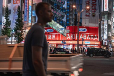 Akihabara, Tokyo 'daki neon reklam panoları GiGO atari salonunda toplanıyor. Bulanık bir yolcu ve önplandan geçen küçük bir kamyon, gece hayatı enerjisini yakalıyor..