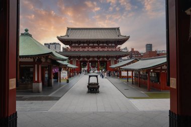 Ziyaretçiler Asakusa, Tokyo 'daki Senso ji' de toplanarak Hozomon kapısına bakıyorlar. Yeşil kiremitler ve kızıl salonlar avluda hizmete hazır, sıcak bir akşamda bir servis arabası yolda dinleniyor..