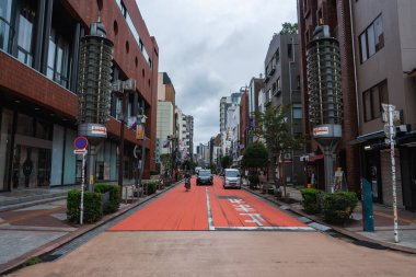 Tokyo tarafında kırmızı bir otobüs şeridi, koyu beyaz kanji, orta yükselen tuğla ve beton binalar, lamba kuleleri, hafif trafik ve hafta içi sakin şehir merkezi olan bir cadde uzanır..