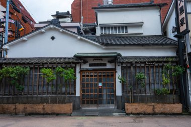 Tokyo 'da beyaz alçılı, kiremit kaplamalı, kafes pencereli ve saksı bitkileriyle geleneksel bir ev sakin bir caddenin yanında duruyor. Kapalı bir ryotei kapısı yerel günlük yaşamı işaret ediyor..