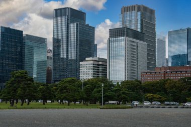 Ağaçların arkasından cam ve çelik kuleler yükselir ve Tokyo Marunouchi 'de İmparatorluk Sarayı yakınlarındaki çakıllı merdivenler. Parkland, arabalar ve ofisler açık gün ışığında buluşur.